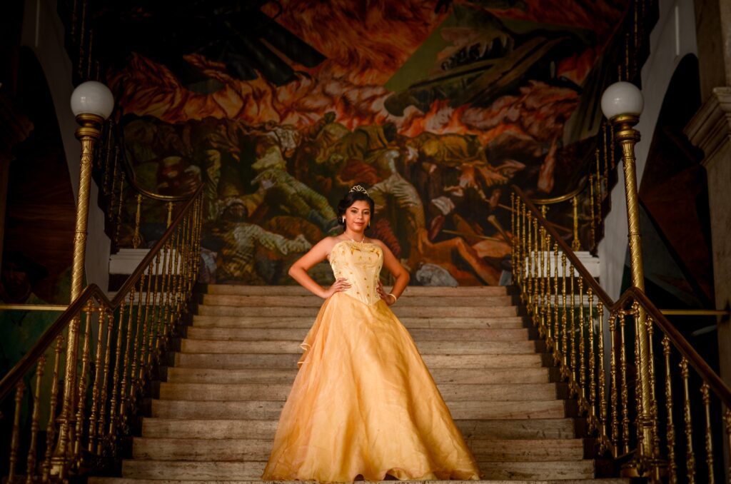 Girl in a big yellow ball gown coming down the stairs wearing a tiara
