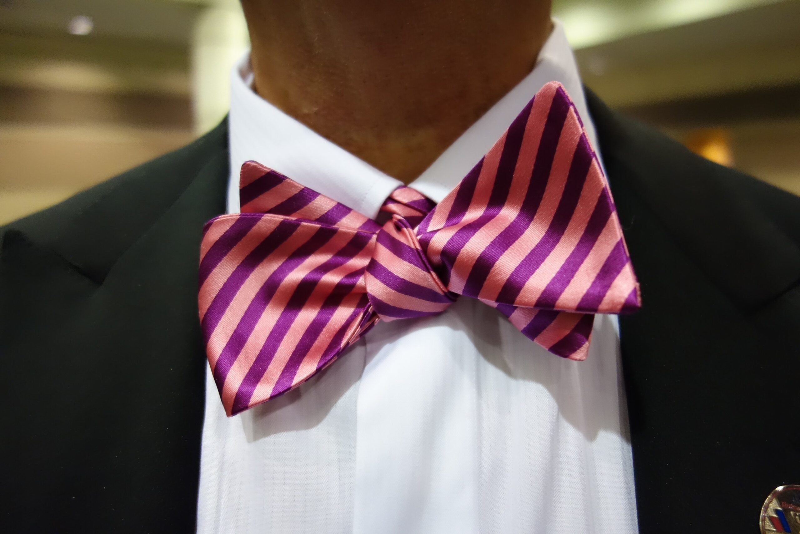 Image of Man wearing a suit and white shirt with colourful pink and purple bow tie around his neck.