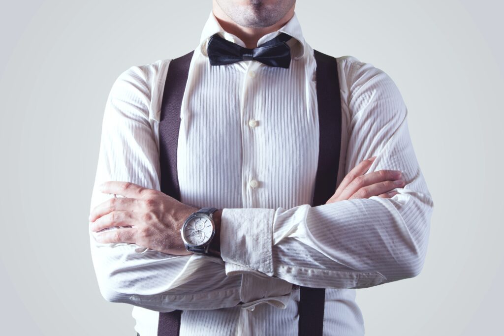 Man With Both Hands on Arm wearing suspenders and a bow tie.