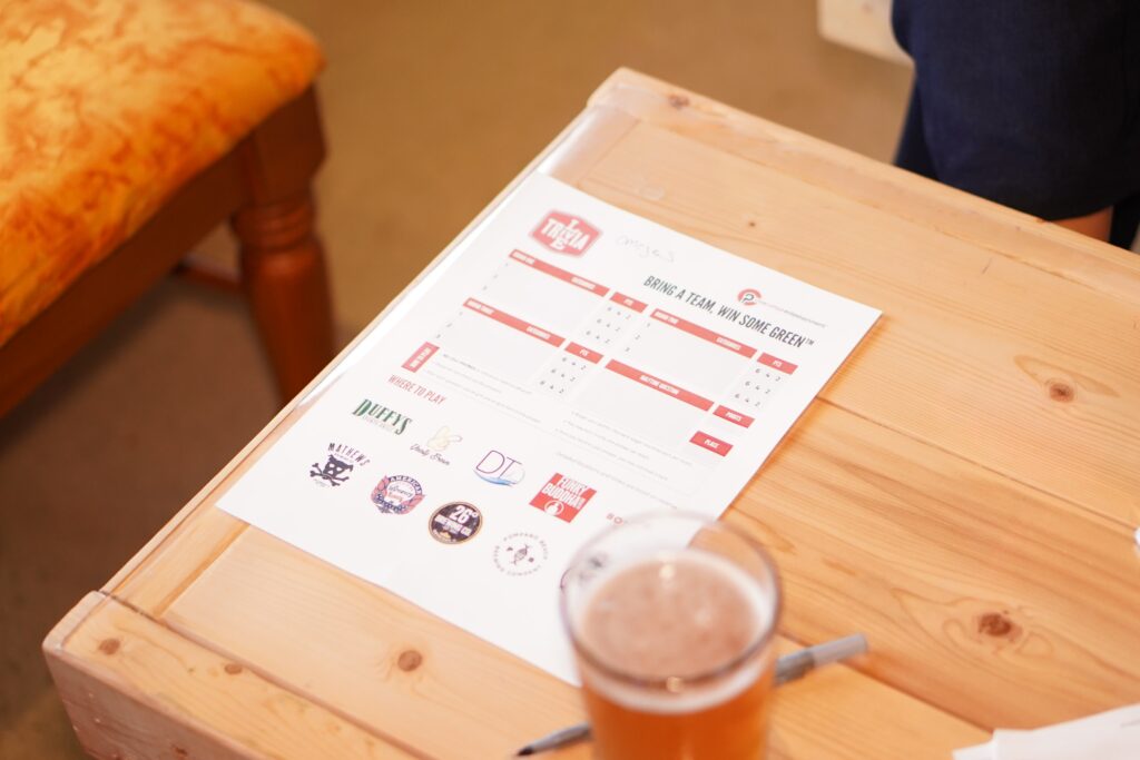 Trivia Night at Yeasty Brews photo shows a sheet of paper with a quiz on the page with logos and a pen on the side of the table and a beer 