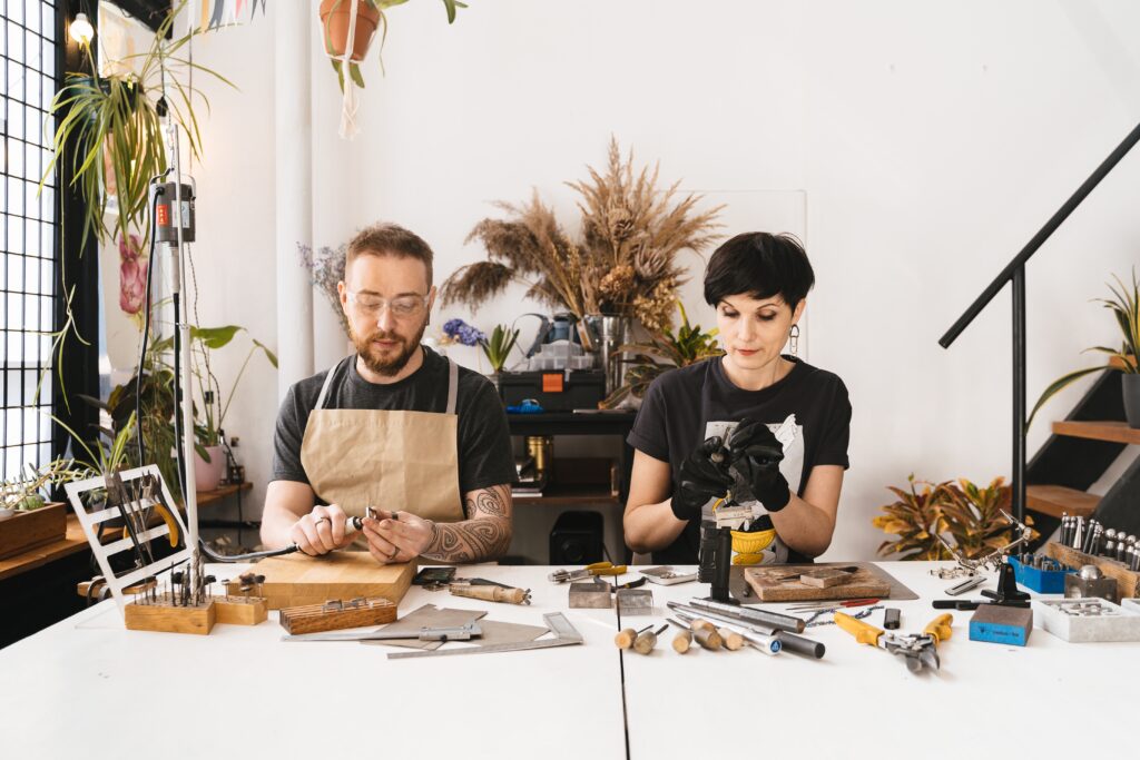 Man in Black Shirt and Brown Apron Sitting Beside a Woman in Black Shirt both doing crafts projects