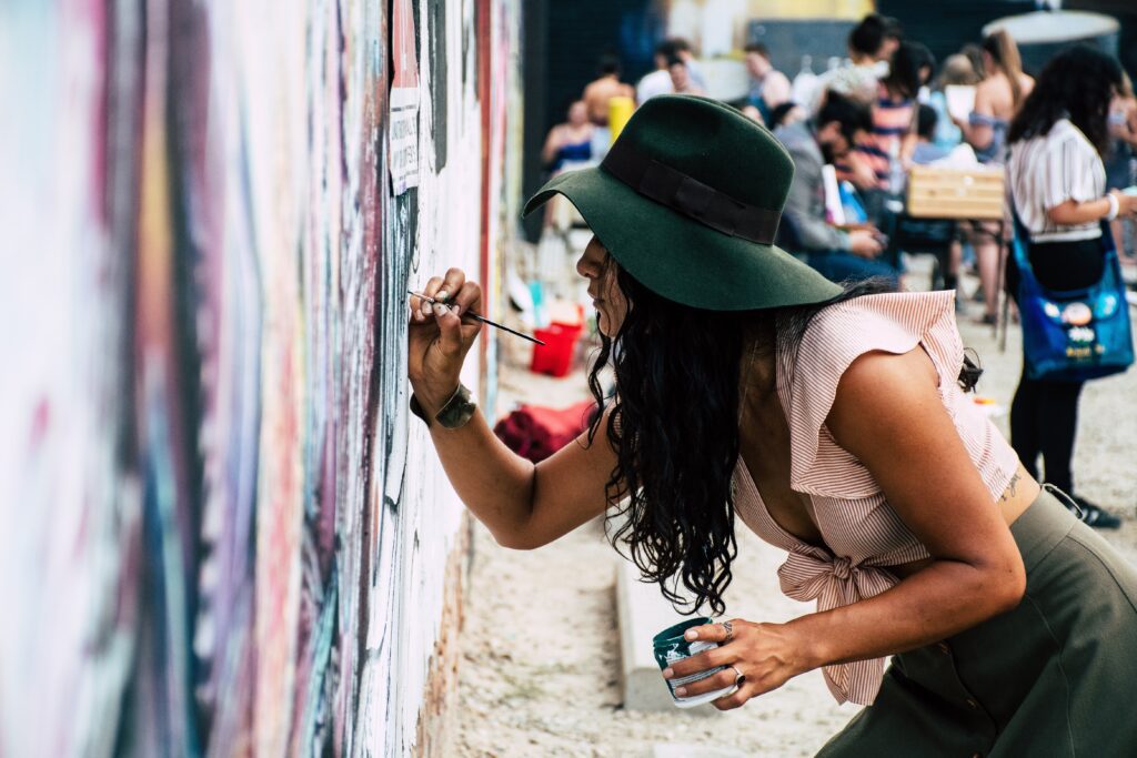 Photo of Woman Painting on Wall wearing a hat and holding a pot of paint participating in this activity during an event