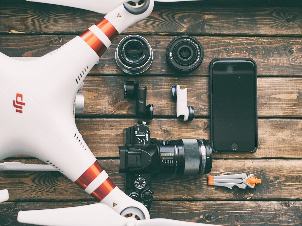 Drone, camera, lenses, smartphone and pocket tools on a wooden table.