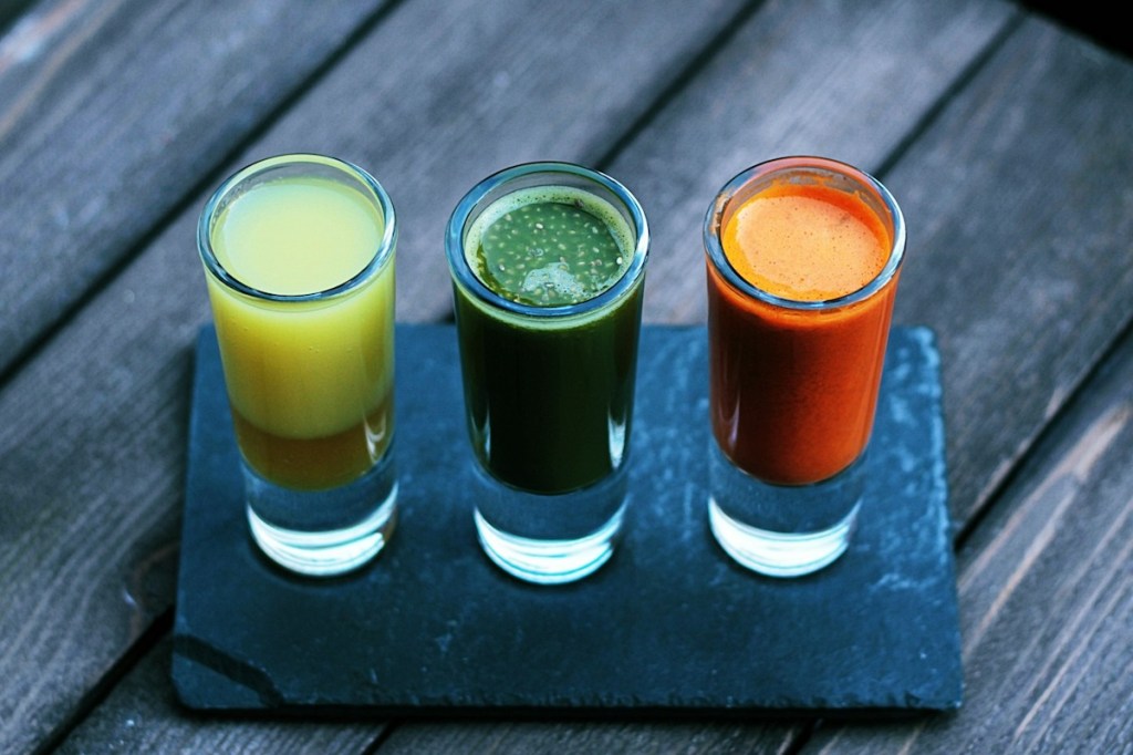 Three clear shot glasses on black slate filled with colorful juices