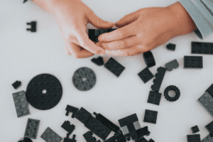 Small child hands playing with black lego blocks on a white table