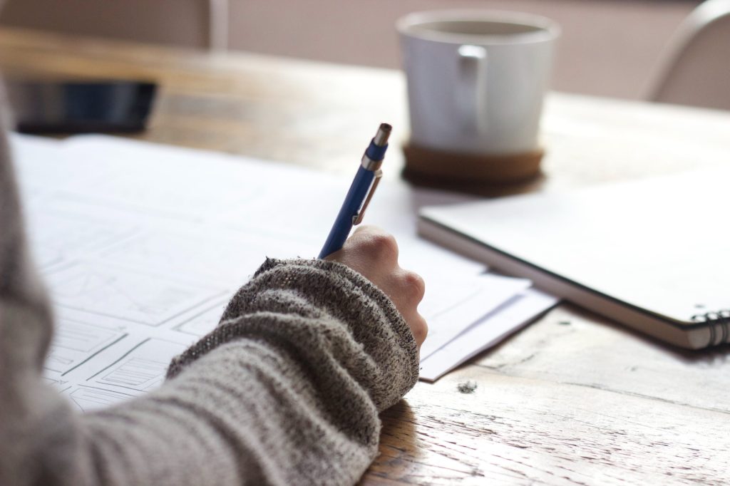 A close up shot of an event planner's hand holding a pen above a stack of papers, including checklists.
