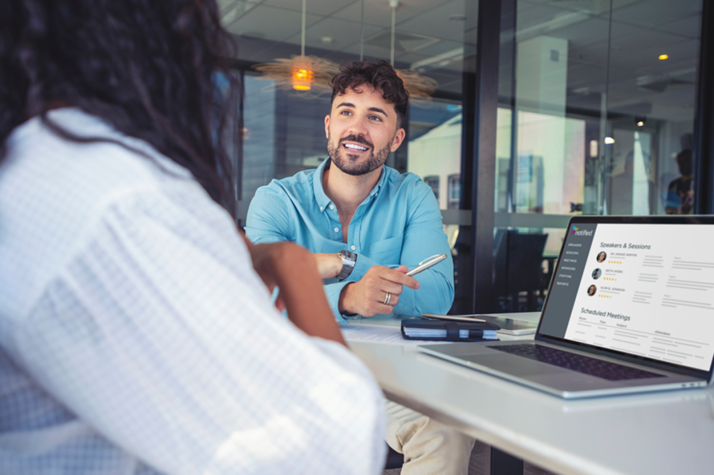 Two event managers sit side by side discussing efficiency hacks in front of a computer.