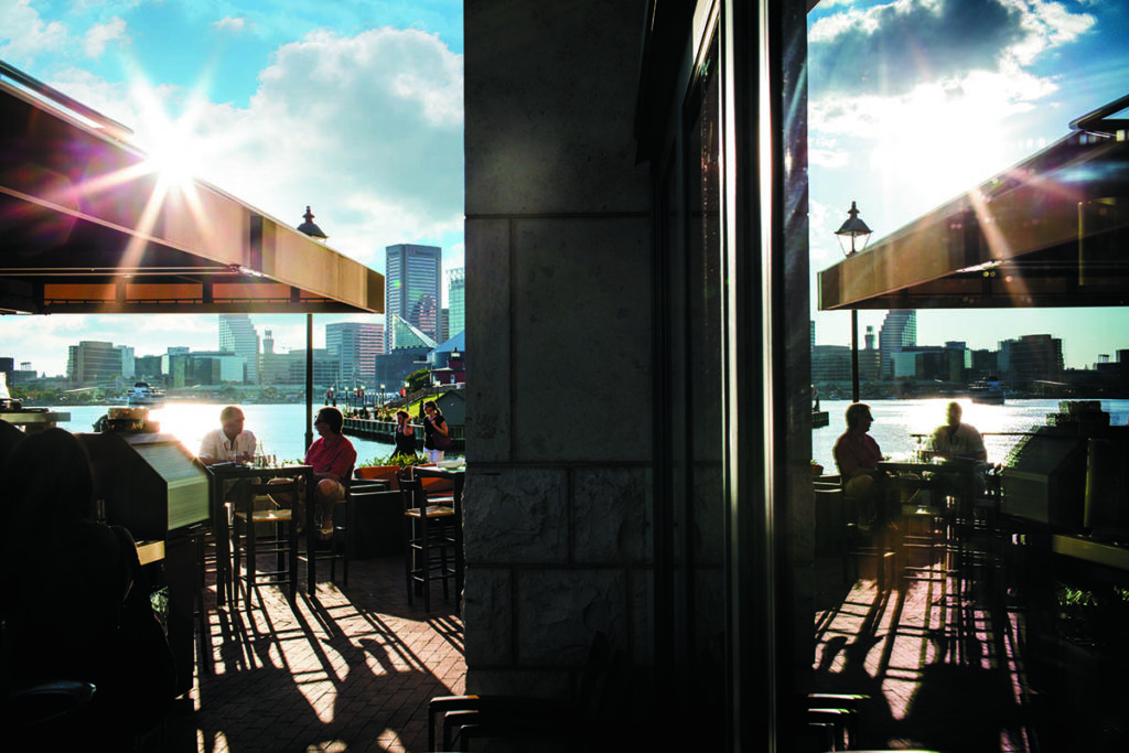 Two people sit on a restaurant patio overlooking Baltimore's picturesque waterfront, a great option for planners looking event destinations with outdoor dining locations.