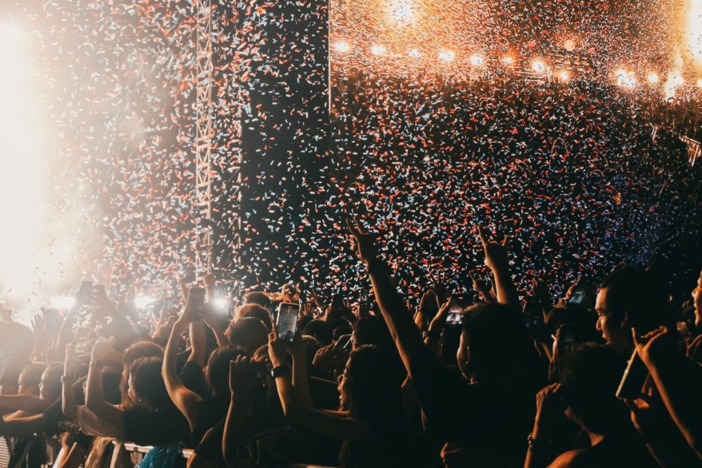 Crowd at an event with their hands up facing towards a strage with confetti in the air