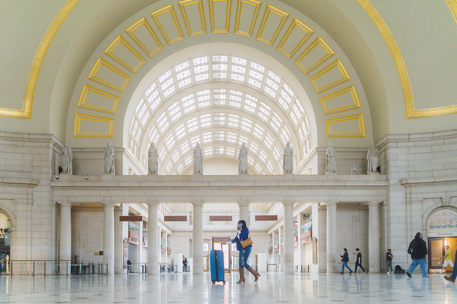 An interior shot of Washington DC's Union Station showing an arched walkway with a skylight overhead and several passengers walking by.
