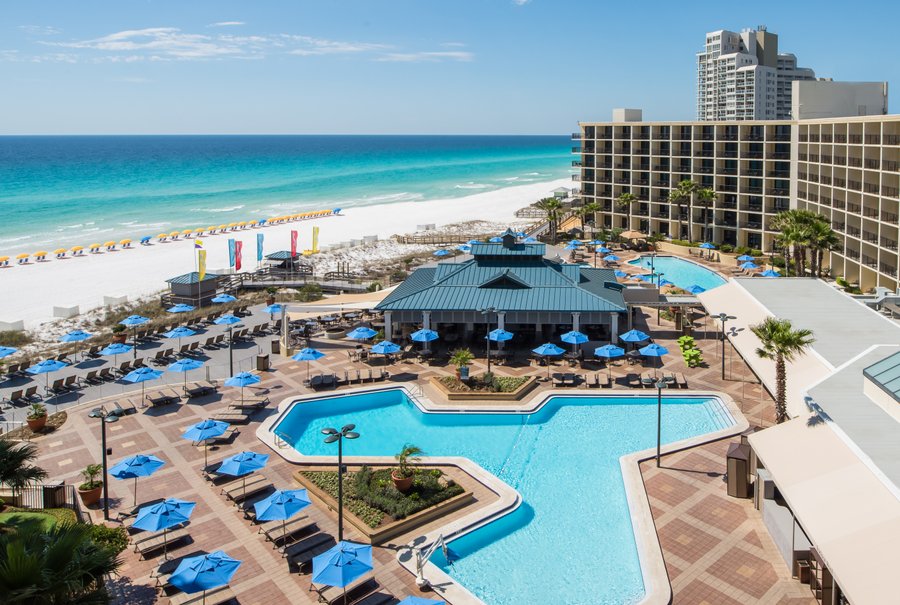 An exterior shot of the Hilton Sandestin Beach Golf Resort & Spa, with a view of its inner courtyard complete with two pools and a view of the white-sand beach.