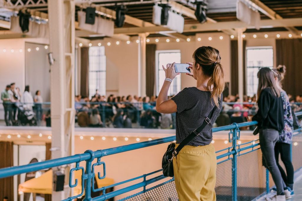 Attendees at a business event watch the show floor from an overhead gallery, with an audience attending an in-person event session in the background.