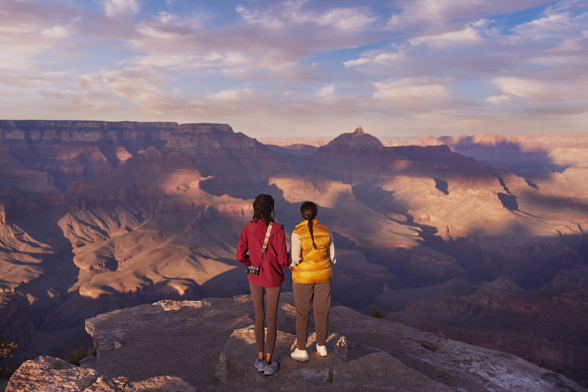 Two figures are seen from behind, standing on a cliff edge overlooking the Grand Canyon in Arizona as part of a group activity to help fight digital burnout.