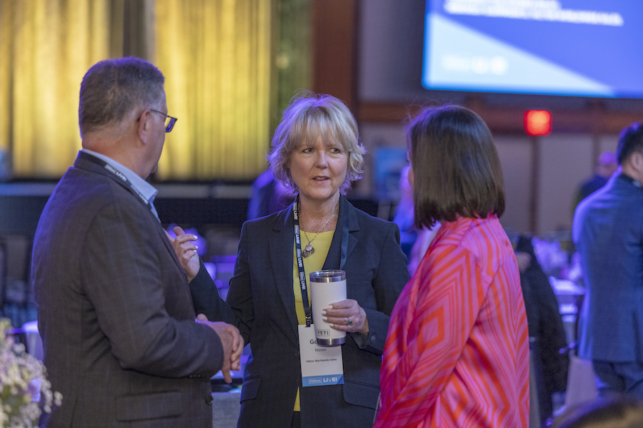 Gerilyn Horan, VP of Group Sales and Strategic Accounts for Hilton, talks to a woman and a man in the banquet hall of a business event, where she is networking to help attract new talent to event jobs.