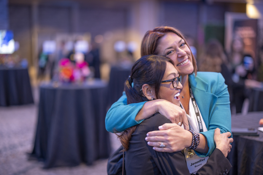Two young women, who are both event professionals, hug each other as they reflect on one of the major career advantages of a job in events: finding your work family.