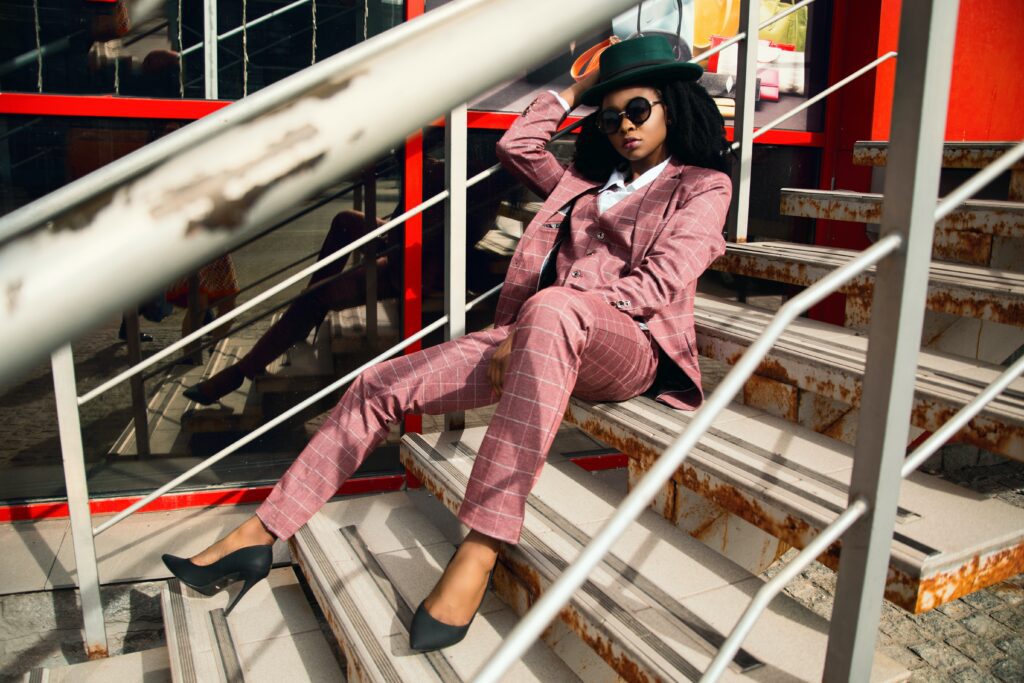 Woman in a bowler hat and heels wearing a pink matching suit set resting on a staircase