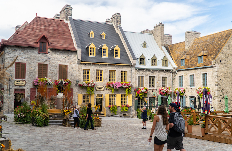 A quaint 17th-century-style square with grey stone buildings (adorned with window flower pots) and a cobblestone plaza in La Cité-Limoilou, the oldest borough in Québec City.