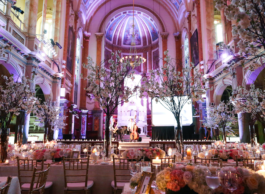 An interior shot of a private event at the Chapelle du Séminaire in Quebec City, with ornate cathedral arches visible in the background and tables decorated with rose bouquets and candles in the foreground.