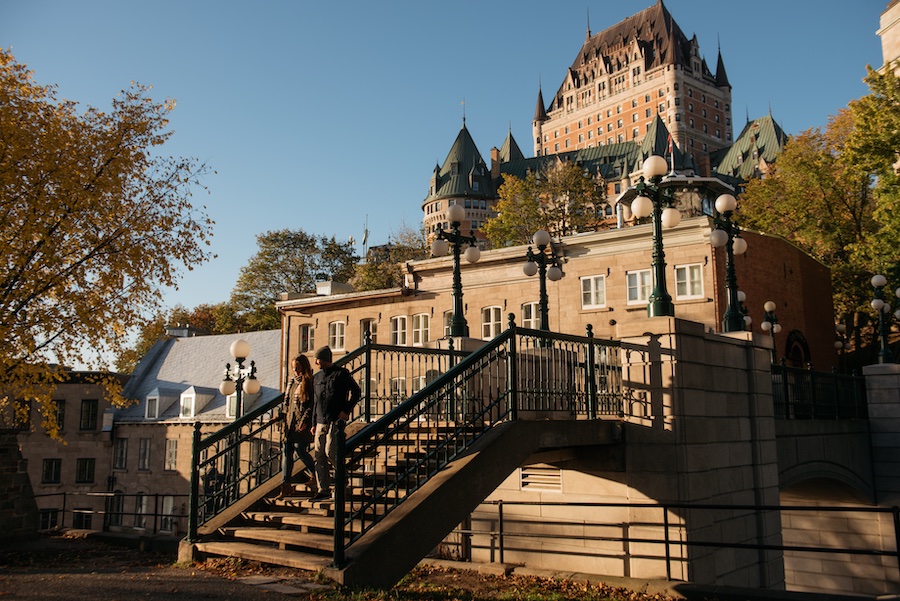 A golden hour view of Parc Montmorency in Quebec City, with a staircase bridge visible in the immediate foreground and The Fairmount Chateau Frontenac visible in the background.
