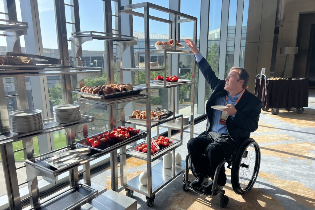 Man in wheelchair reaching for food on high shelf at business event