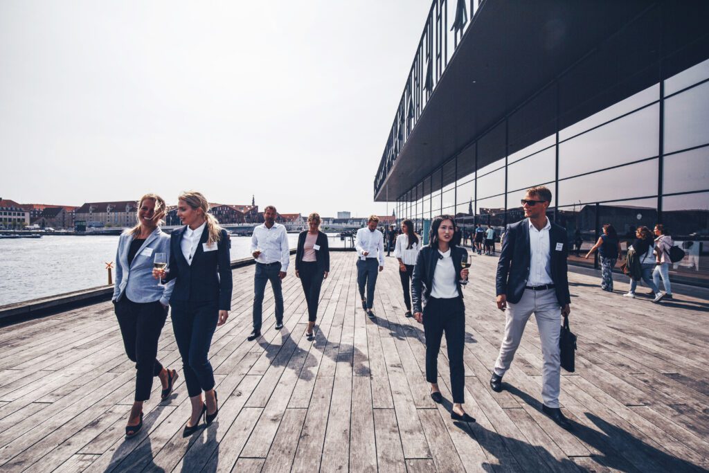 Congress attendees walk along an exterior boardwalk at the Royal Danish Playhouse, with the waterfront to the left and the ultra-modern glass exterior of the building to the right. This congress was part of important research into event legacies.