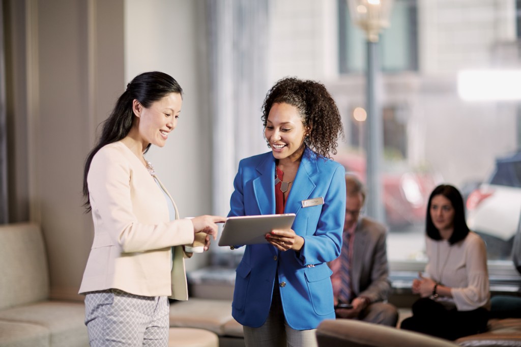 A meeting planner consults with a Hilton sales representative to learn about the Meet With Purpose program and learn how it can help with reaching ESG goals. They are both wearing blazers and looking at a tablet device in what looks like a hotel lobby.