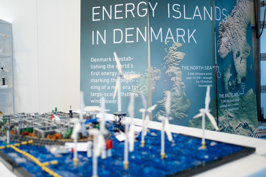 A shot of a poster explaining Denmark's "energy islands" project, featuring a map of Denmark and surrounding countries with markers for the location of offshore wind-energy hubs. In the foreground, an out-of-focus Lego model of an offshore wind farm is visible. This display was part of an event legacy case study.