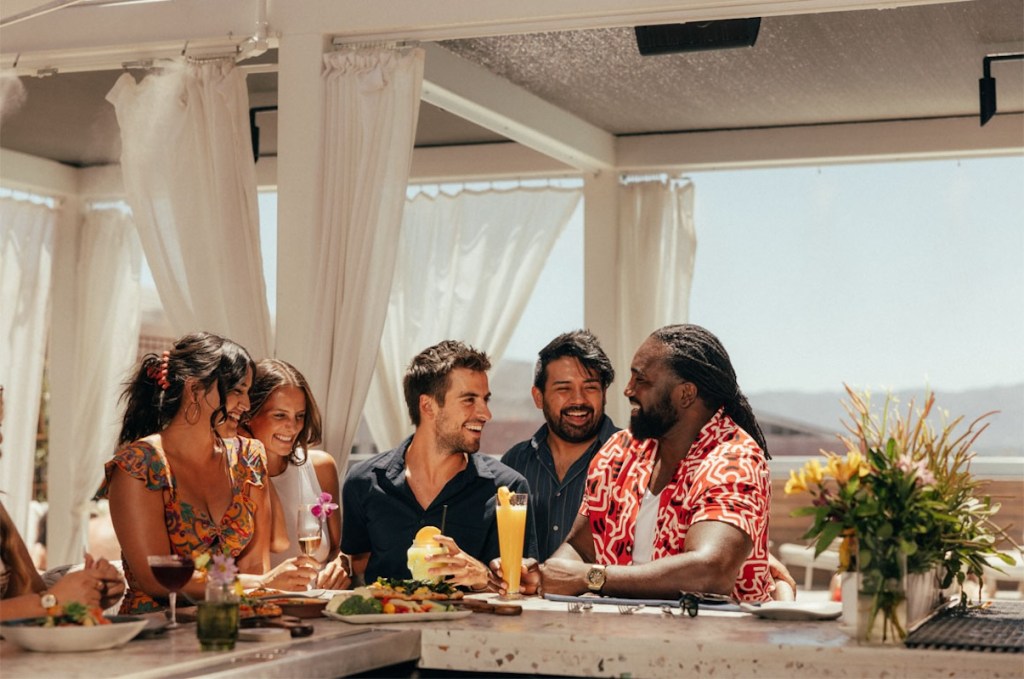 Five meeting attendees dressed in casual summer clothes sit at a bar with columns behind them, and a Phoenix desert vista beyond.