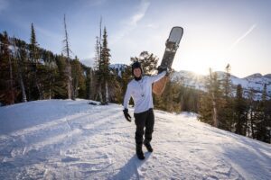 Snowboarder holds snowboard at top of mountain