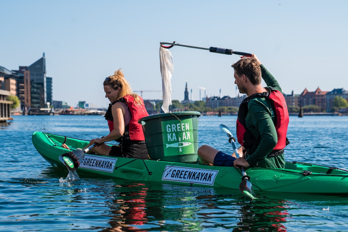 A man and a woman ride together on a kayak using grabber tools to pick up garbage in the water. Tracking these kinds of activities can be key for measuring event legacy success.