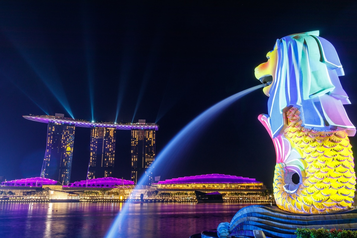 Nigh photo of Singapore's Merlion fountain with bright colorful lights overlooking the Marina Bay Sands
