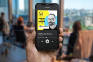 Person in an office holding up a mobile phone with the Skift Meetings Podcast with an episode titles Creating a Target Audience of One featuring Mathias Sondermann