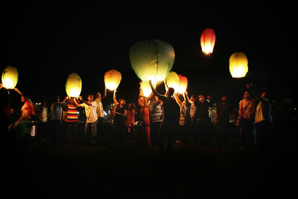A group of people standing in the dark holding up paper lanterns