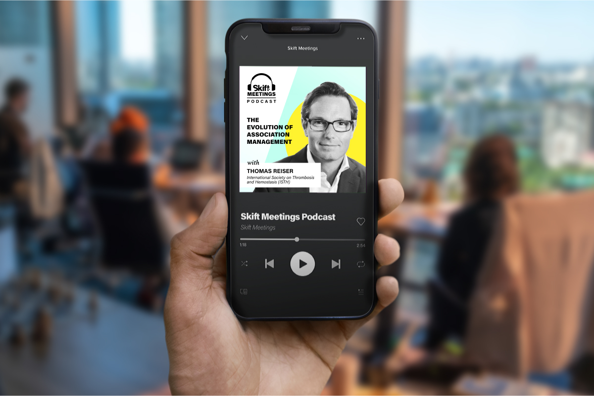 Person holding a smartphone with a podcast app open on the Skift Meetings Podcast featuring Thomas Reiser