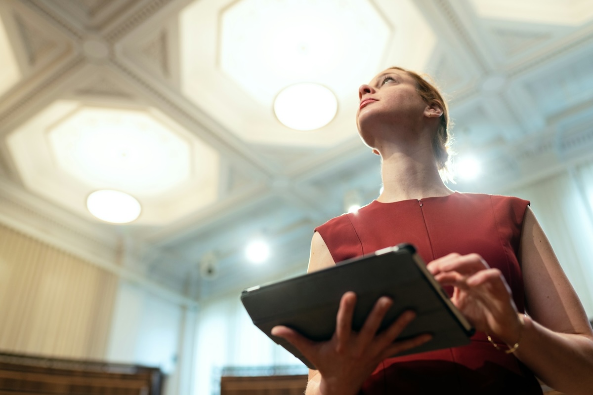 Business woman holding a tablet looking up towards the lights in a hotel ballroom.