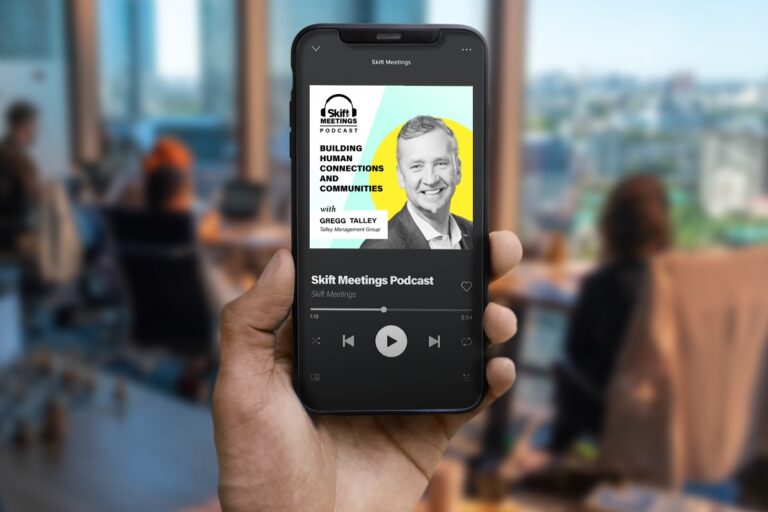 Person holding a smart phone playing the Skift Meetings Podcast featuring Greg Talley