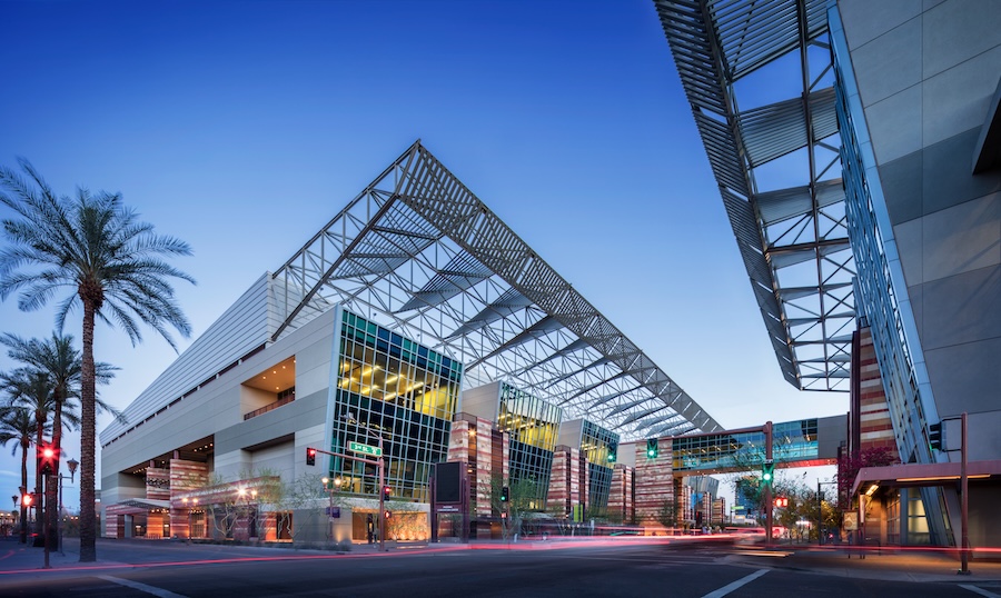 An exterior shot of the Phoenix Convention Center at dusk. The building is divided into two sides, with a wide roadway in between and a glass tunnel connecting the two structures.