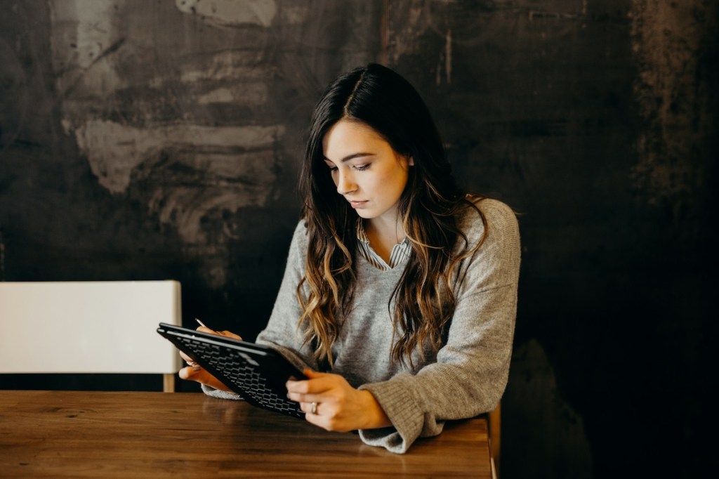 Woman wearing white dress shirt using holding black leather case on brown wooden table