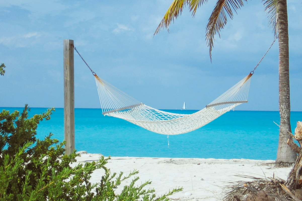 A white hammock on a tropical beach with clear and calm blue sea in the background