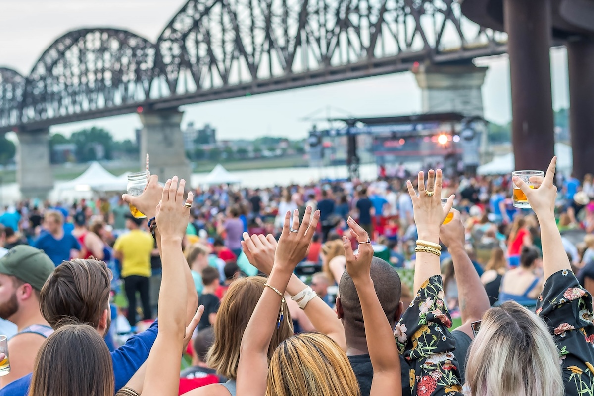 Concergoers cheering a band on stage while holding drinks at the Louisville Waterfront