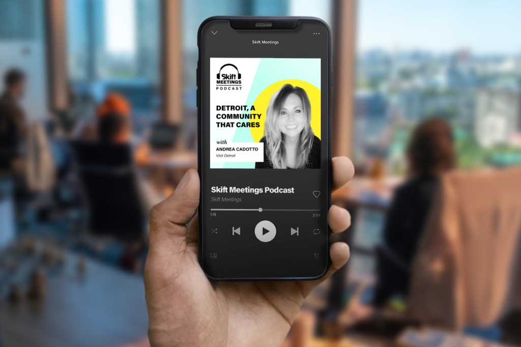 Person holding a phone playing the Skift Meetings Podcast featuring Andrea Cadotto, director of sales at Visit Detroit.