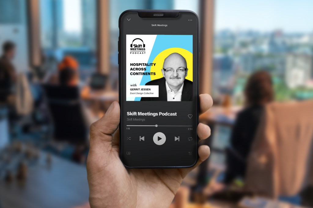 Person holding a smartphone playing the Skift Meetings Podcast, Hospitality Across Continents episode featuring Gerrit Jessen