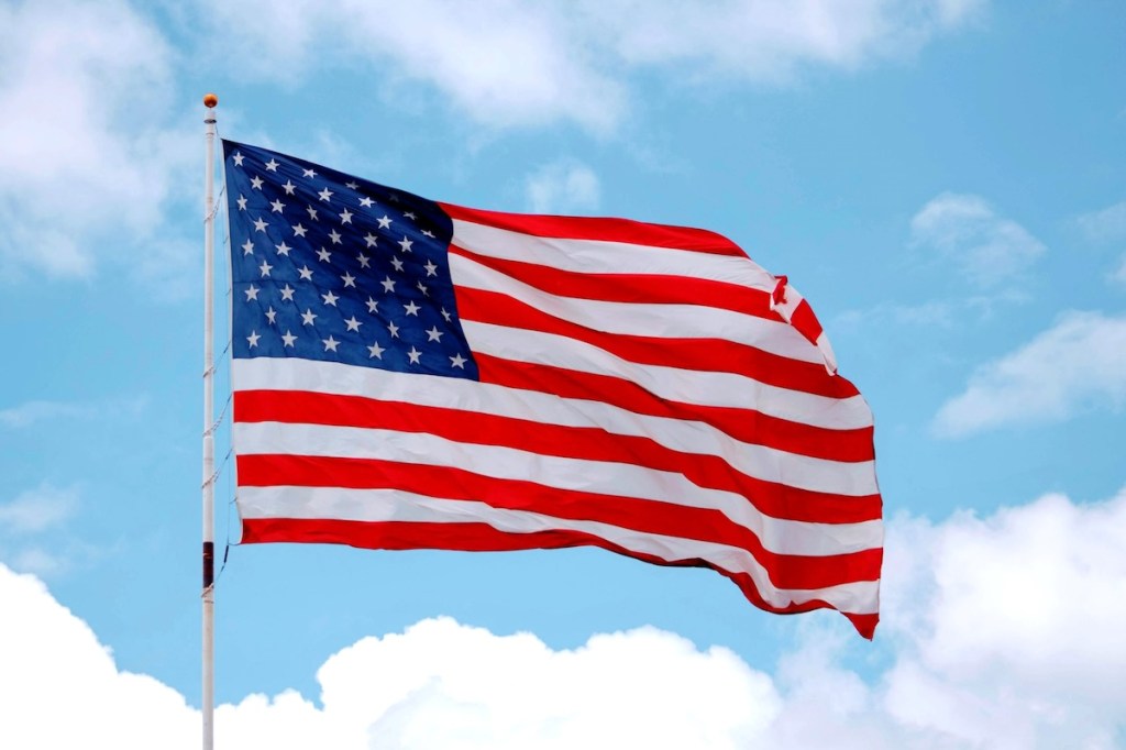 Large American flag with a background of light blue sky and white clouds