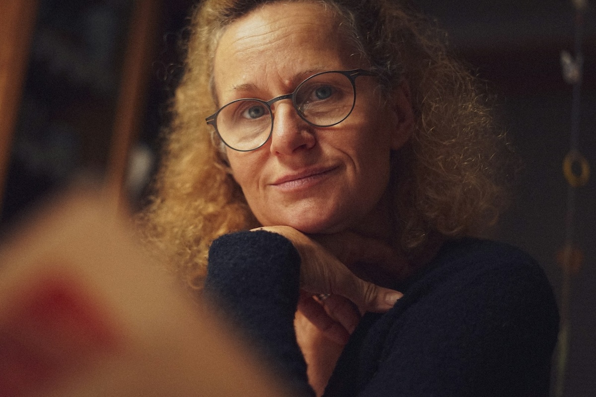 A middle-aged woman wearing glasses indoors in dim lighting