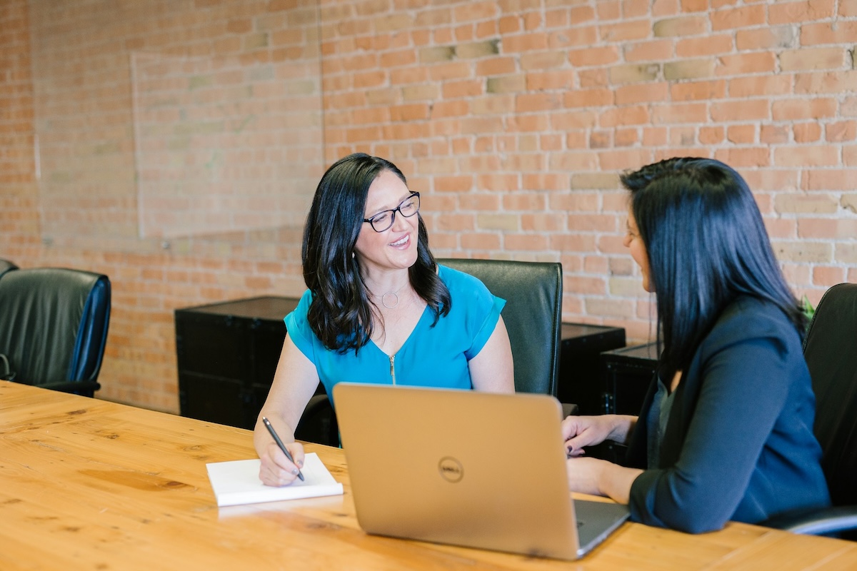 Woman in teal t-shirt sitting beside woman in suit jacket