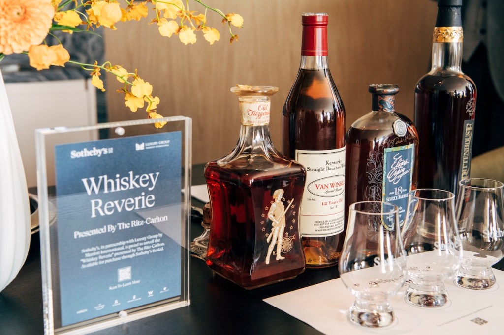 Four bottles of whiskey with corresponding tumblers and a blue sign with the words "Whiskey Reverie"