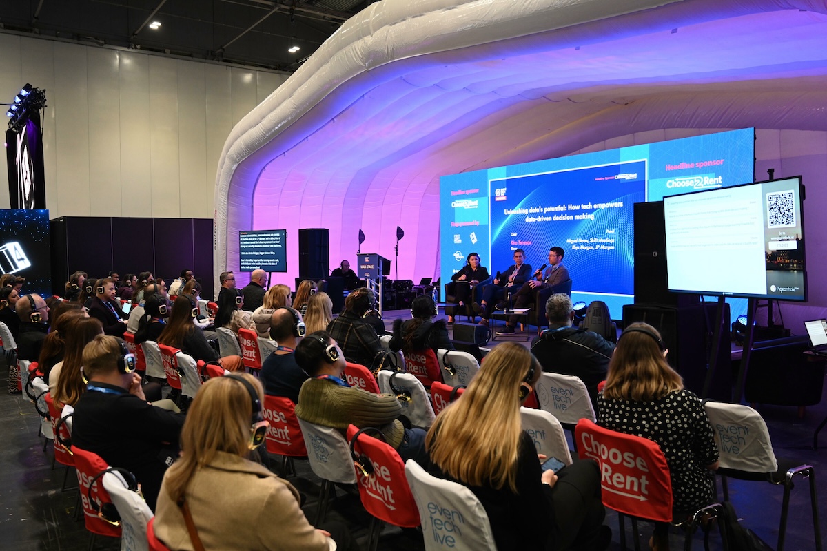 Three people sitting on a stage having a conversation with an audience of around 100 people watching.