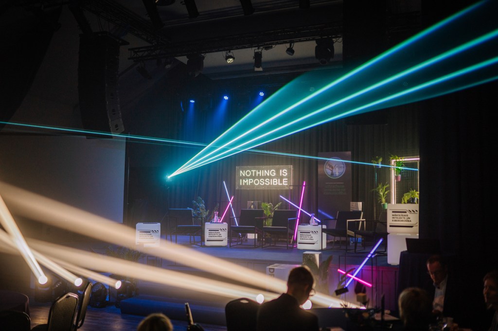 a stage with neon lights and laser beams, featuring a sign that reads “Nothing is Impossible” at a conference event