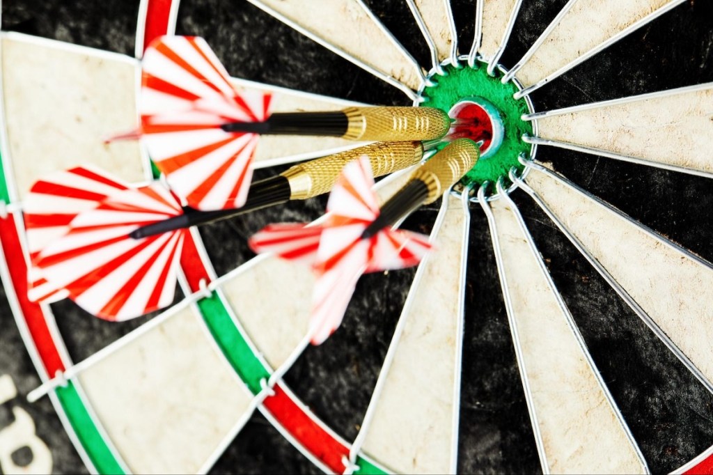 Three darts with red and white flights hit bullseye on dartboard